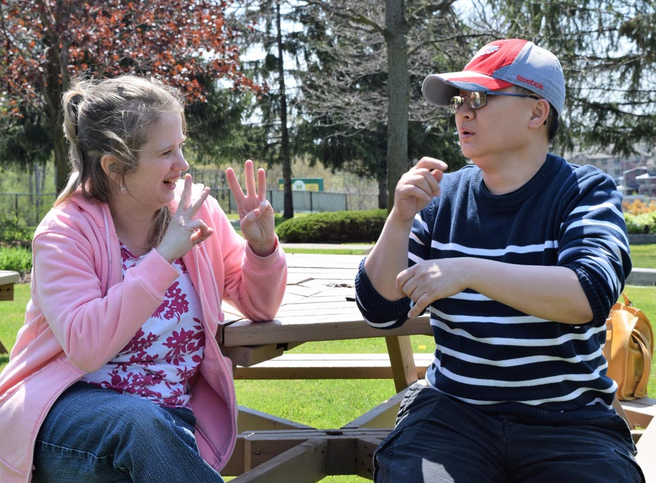 A man and a women sitting outside communicating through sign language