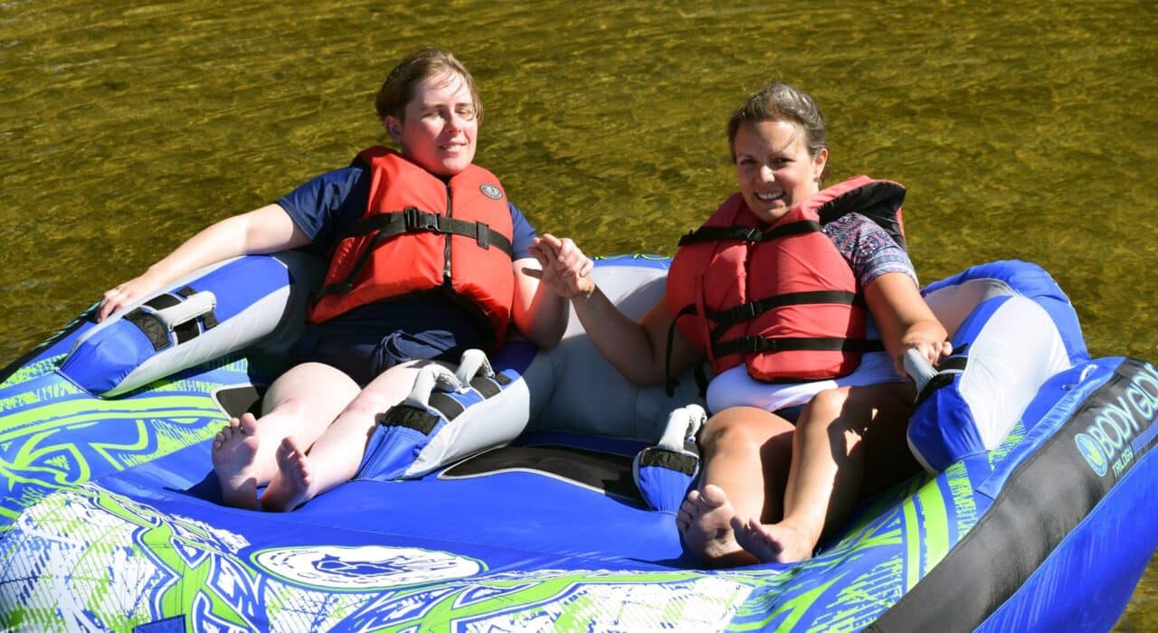 two young woman wearing live jackets sit in a large tube floating in the water