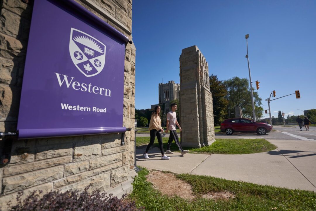 A photo of the outside of Western University. You can see part of the main entrance of the school in the distance. To the left is a purple flag with the Western Crescent and Logo.
