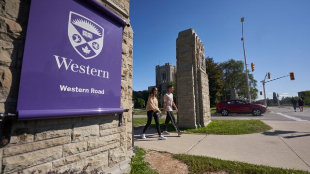 A photo of the outside of Western University. You can see part of the main entrance of the school in the distance. To the left is a purple flag with the Western Crescent and Logo.