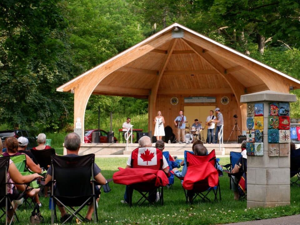 The stage in Paris Lions park featuring a live band playing music. There is a series of lawn chairs facing the stage and a crowd of people watching the show.