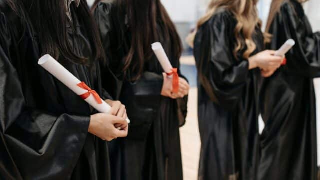 Graduates are holding their diplomas. You can only see the gowns and diplomas in the photo.